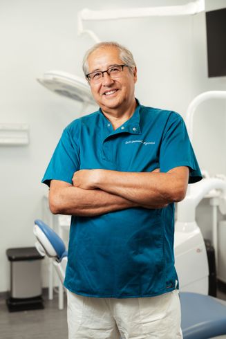 Uomo sorridente con camicia color verde acqua in piedi con le braccia incrociate in uno studio dentistico.
