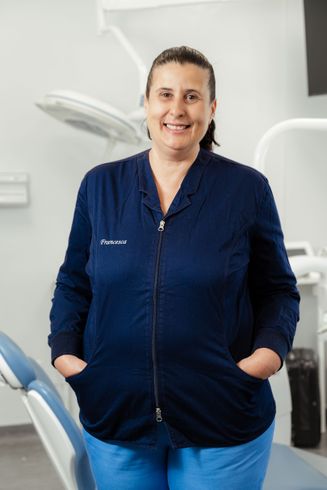 Persona in piedi in uno studio dentistico, con indosso una camicia blu scuro e le mani in tasca.