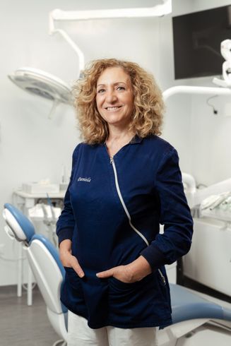 Un dentista sorridente in camice blu scuro è in piedi in una moderna sala visite.