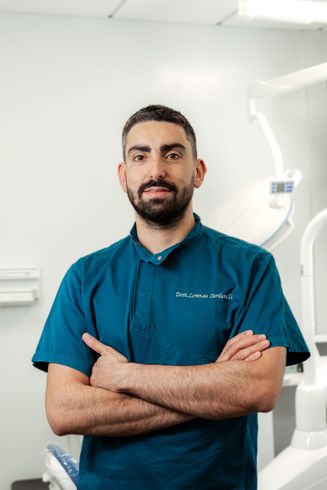 Ritratto di un medico in camice color verde acqua, in piedi con le braccia incrociate in un luminoso studio medico.