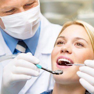 Dentist examining woman's teeth with instruments in a dental office.