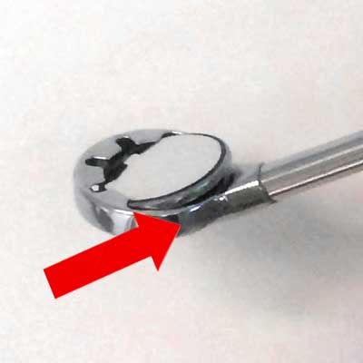 A dental mirror tool with a red arrow pointing to its edge.