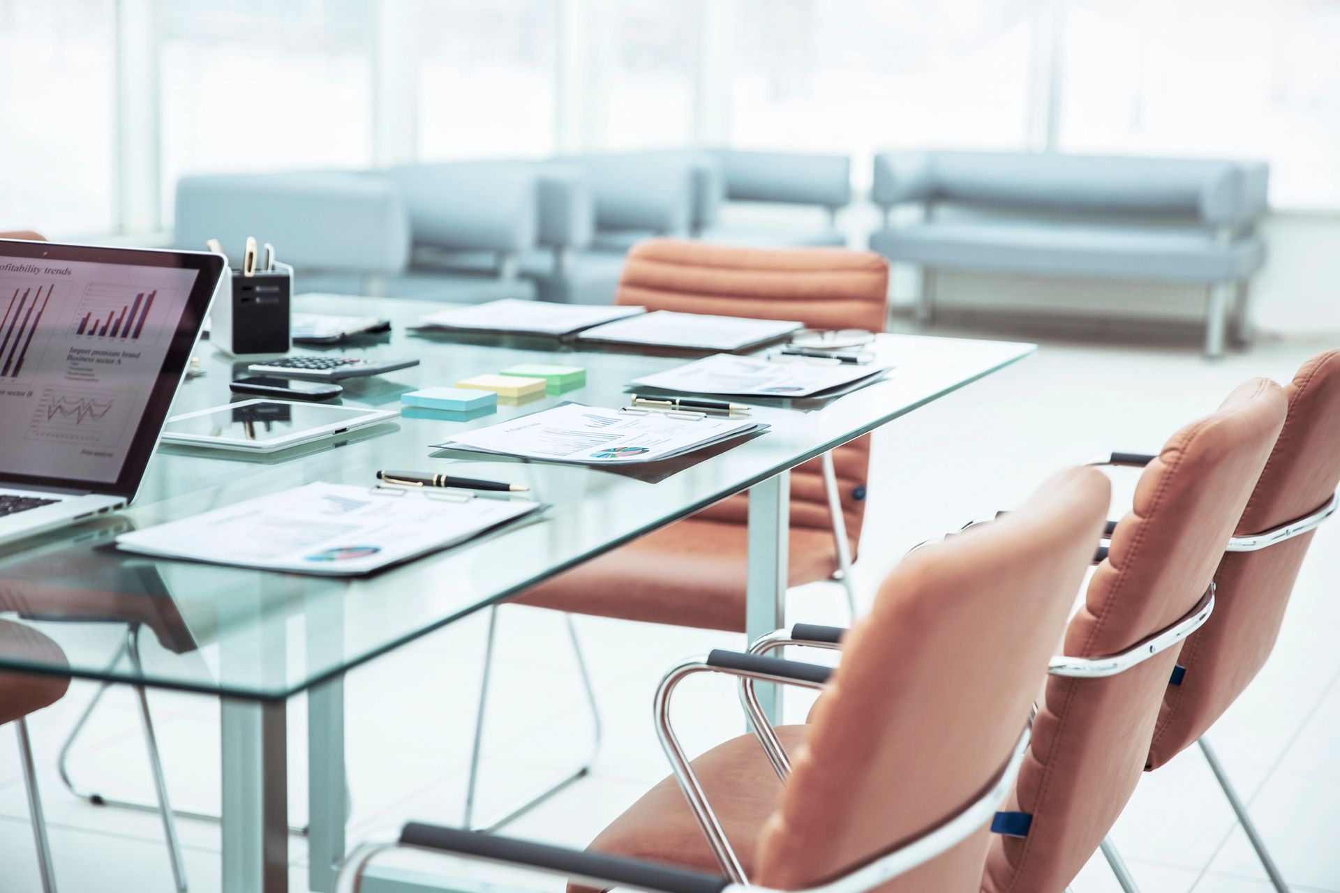 Una sala de conferencias con una mesa de cristal, sillas y una computadora portátil encima.