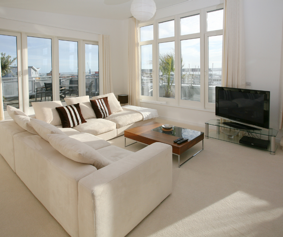 Salon lumineux et moderne avec de grandes fenêtres, un canapé blanc et une télévision.