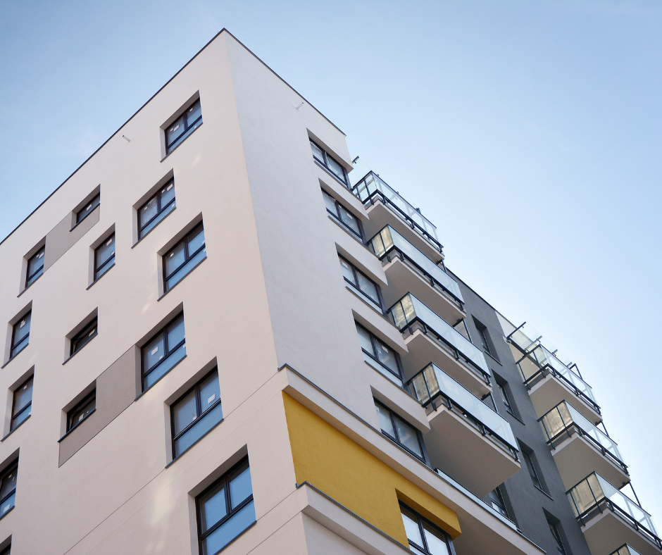 Immeuble d'appartements moderne de grande hauteur avec balcons, façade grise, blanche et jaune sur fond de ciel bleu.