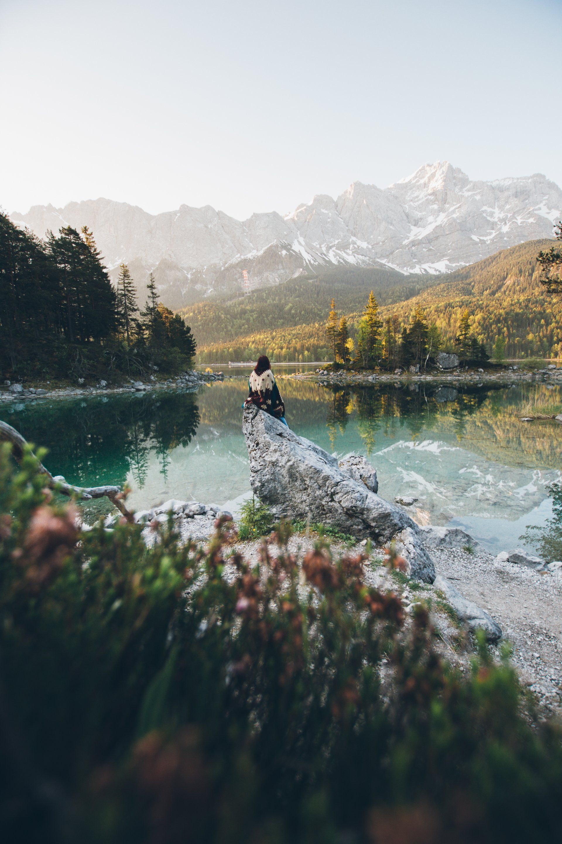 Person sitzt auf einem Felsen neben einem blaugrünen See, im Hintergrund Berge.