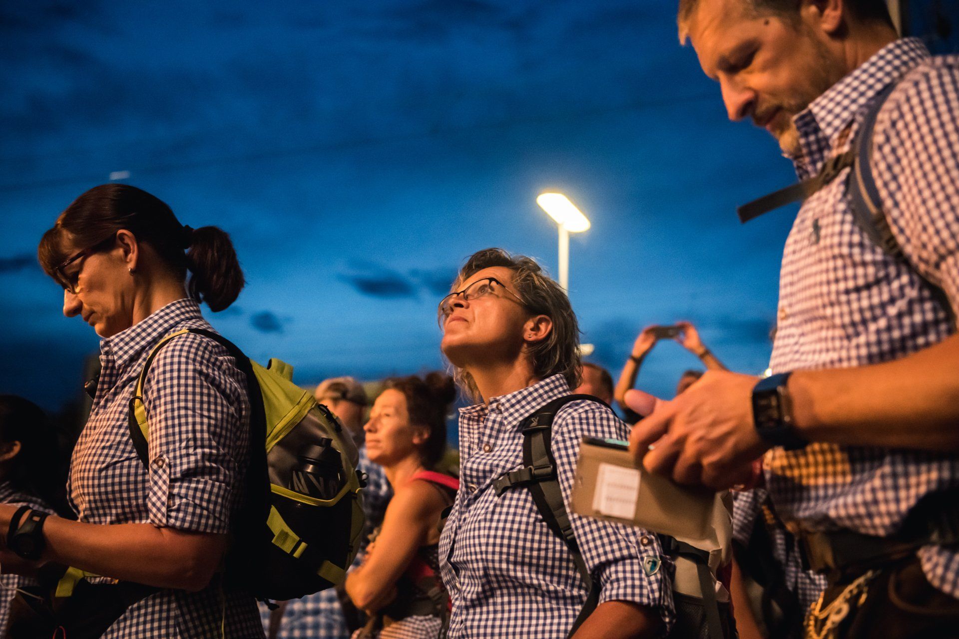 Menschen schauen in den Nachthimmel, manche halten Geräte, möglicherweise zum Sternegucken. Dunkelblauer Himmel.