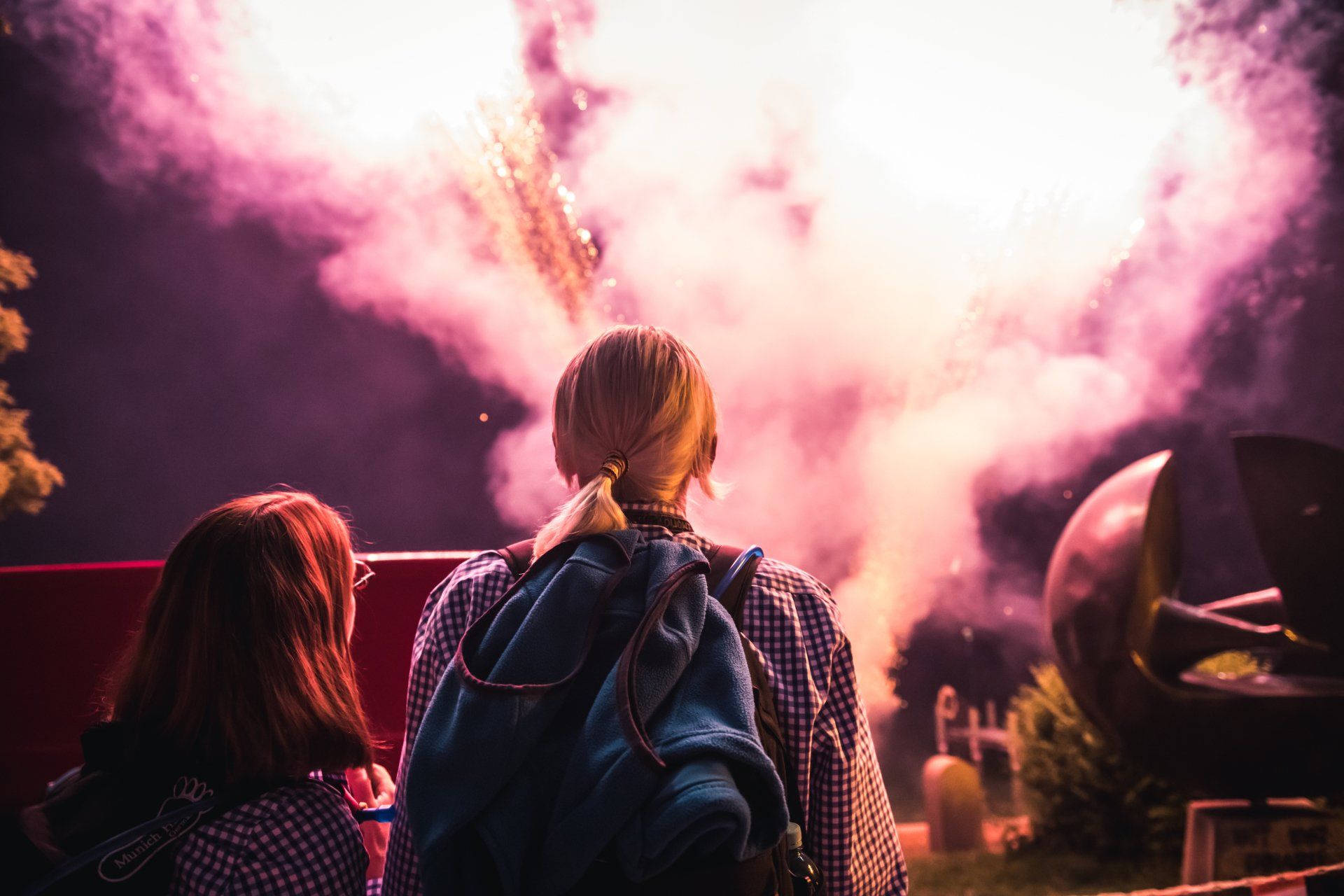 Zwei Personen beobachten nachts, wie ein Feuerwerk in einer rosa-weißen Wolke explodiert.