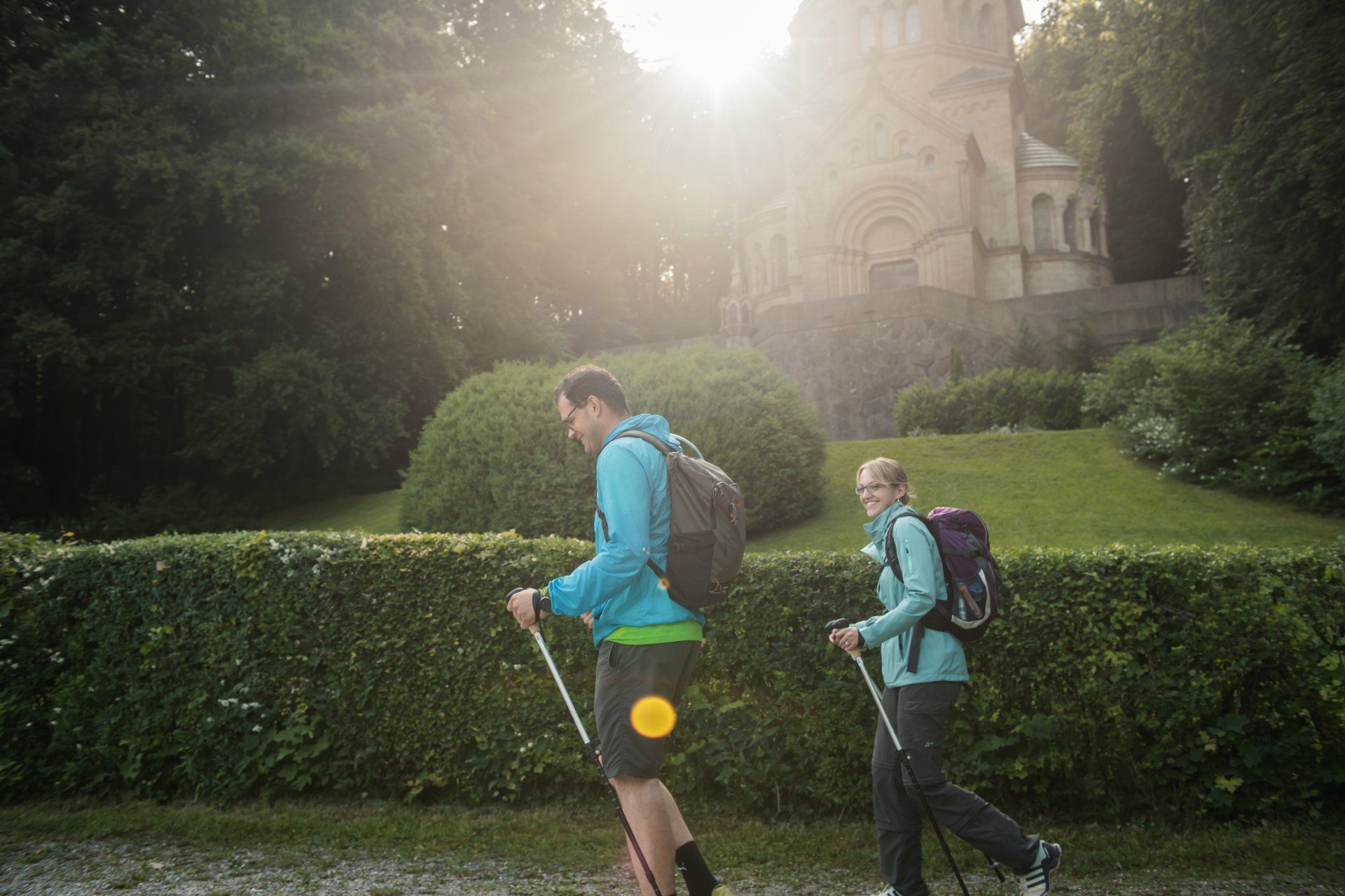 Paar wandert mit Stöcken in der Nähe einer Kirche im Sonnenschein.