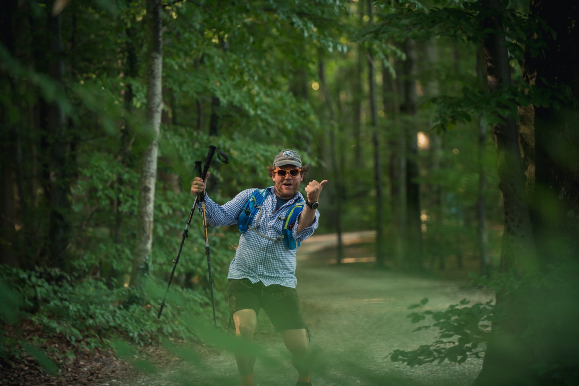Mann läuft im Wald und gestikuliert mit Sonnenbrille und Wanderstöcken.