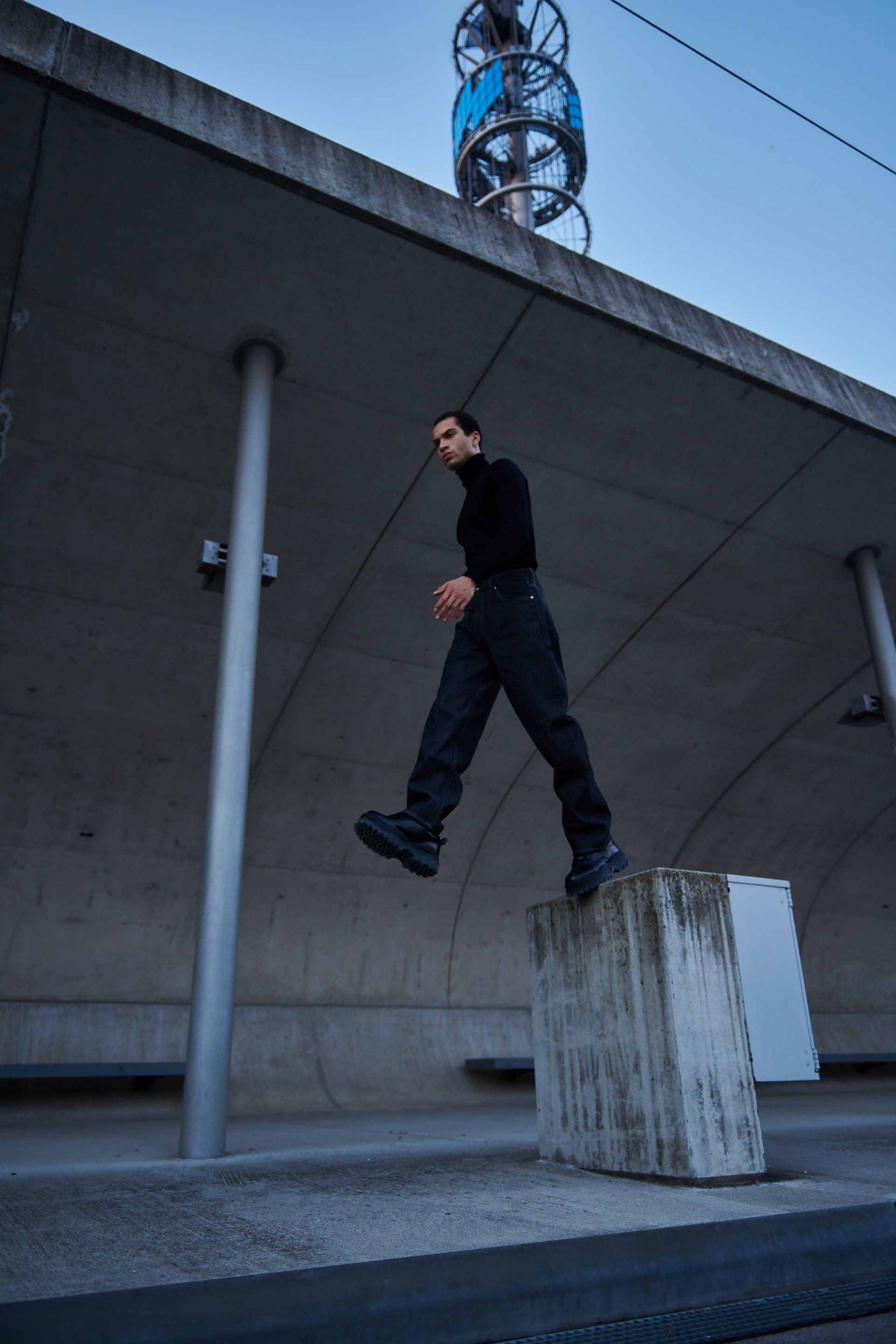 Mann in schwarzer Kleidung tritt im Freien auf einen Betonblock.