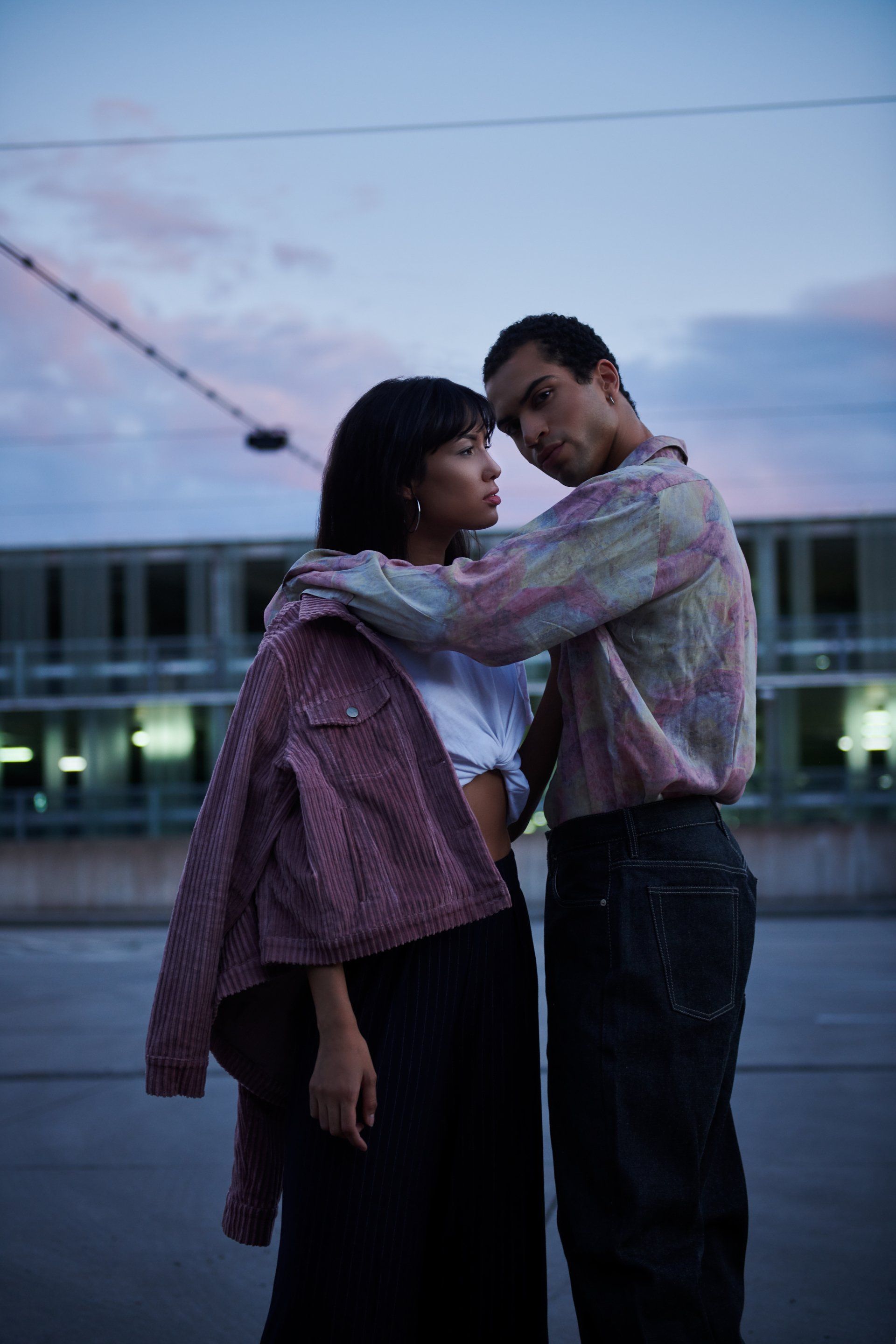 Paar umarmt sich im Freien, mit einem Motel im Hintergrund, in der Abenddämmerung.