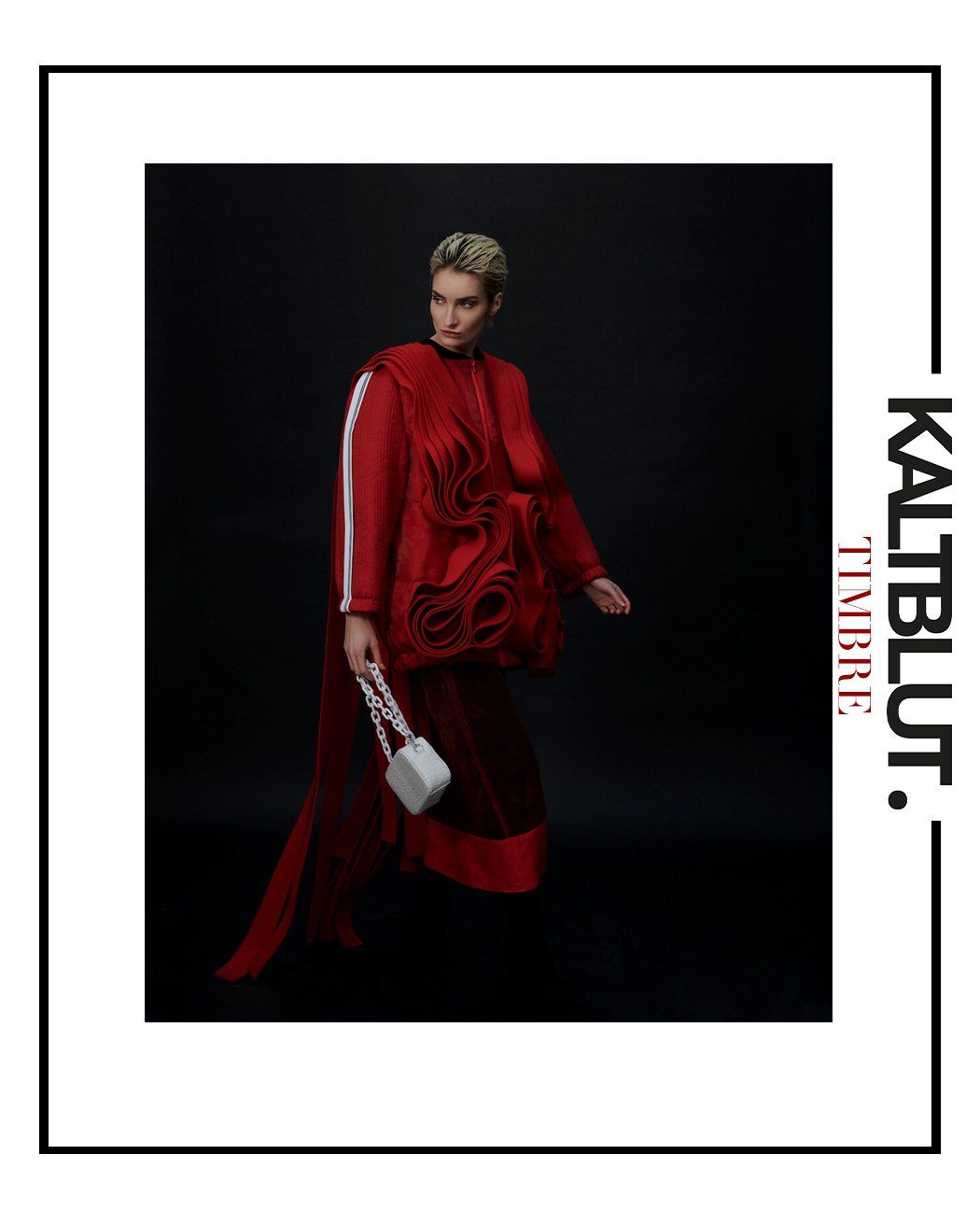 Frau in rotem Outfit vor schwarzem Hintergrund, hält eine weiße Handtasche.