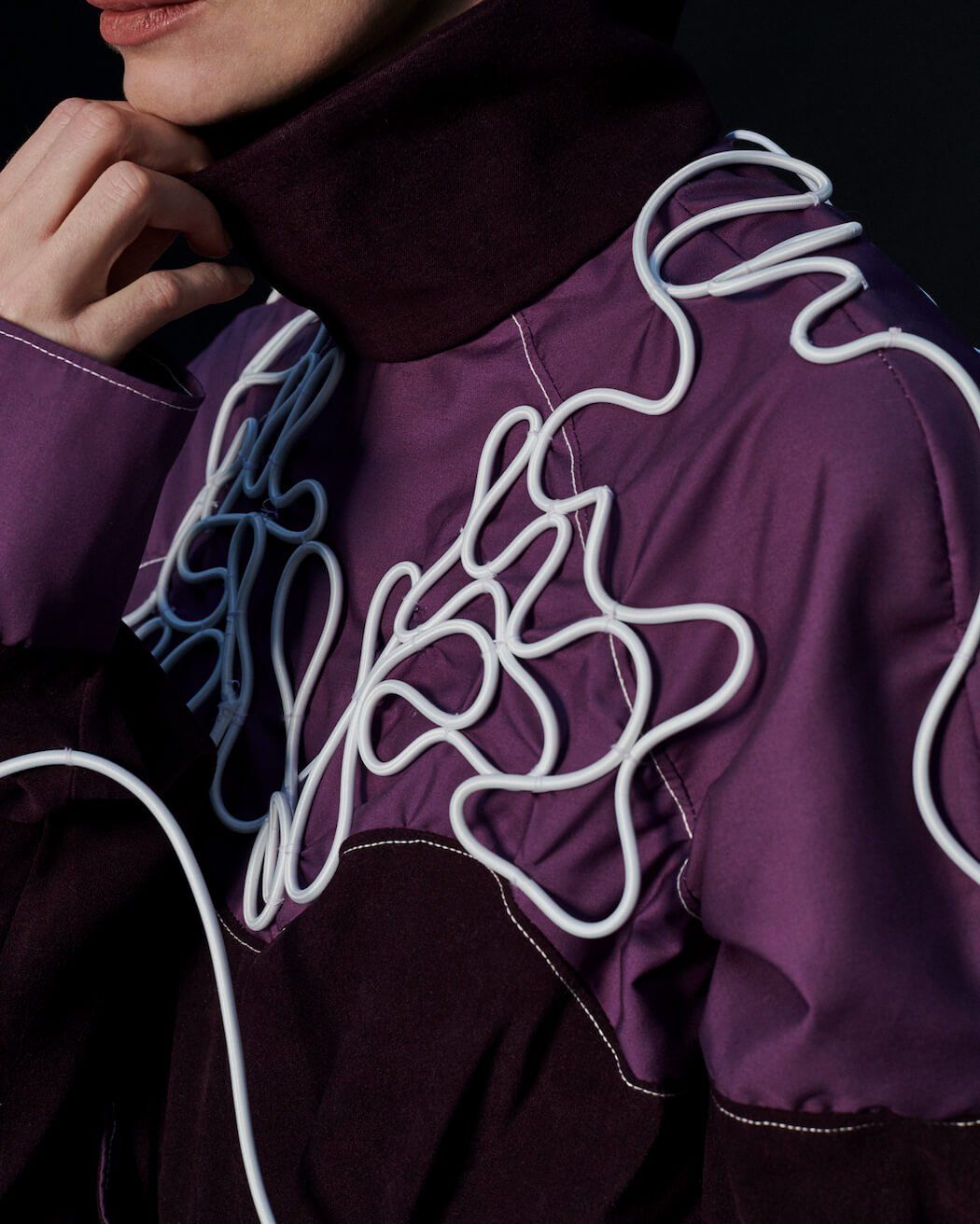 Person in lila Jacke mit weißem Schnörkelmuster und dunkelviolettem Kragen.
