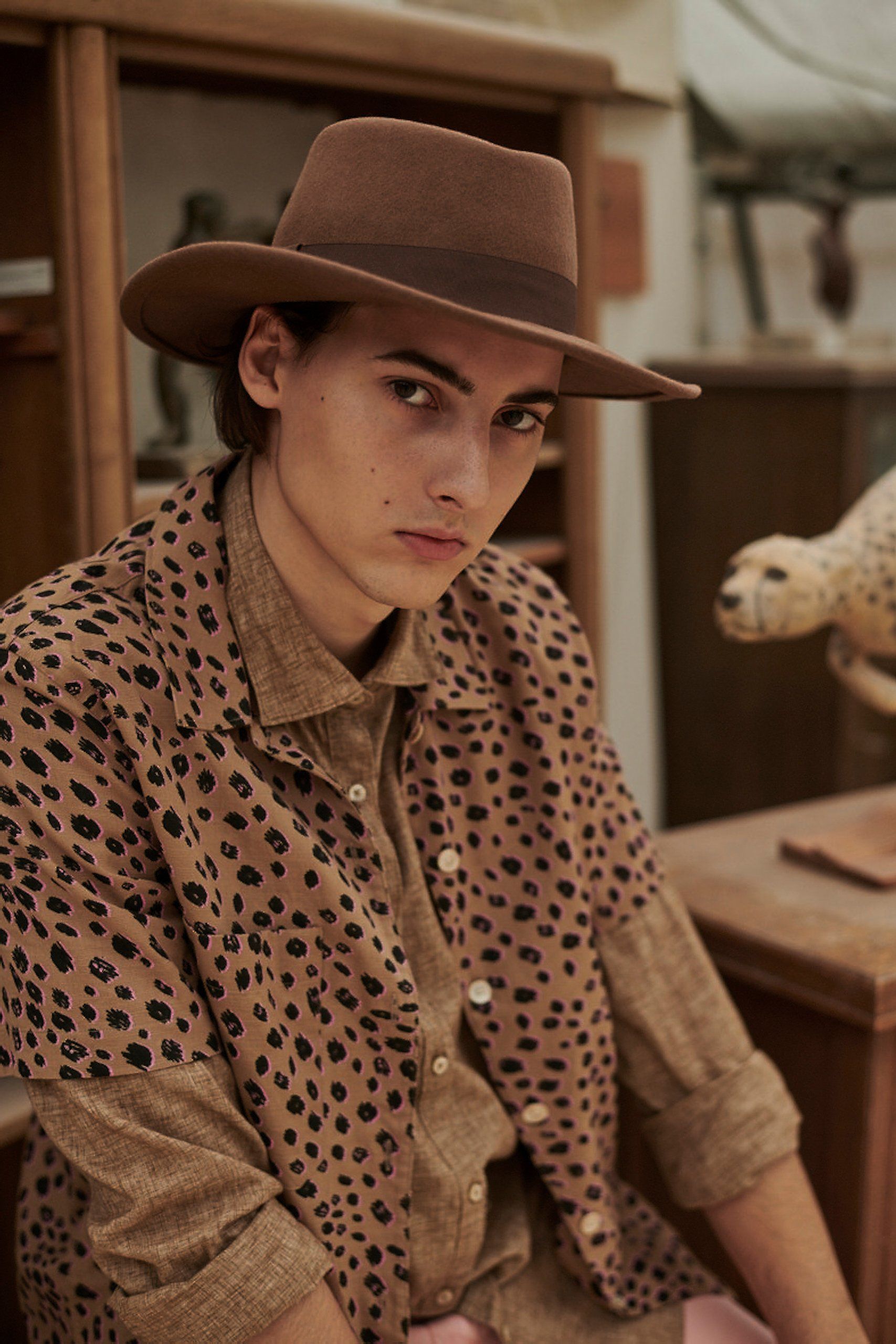 Mann in Hemd mit Leopardenmuster und Fedora, blickt in die Kamera.