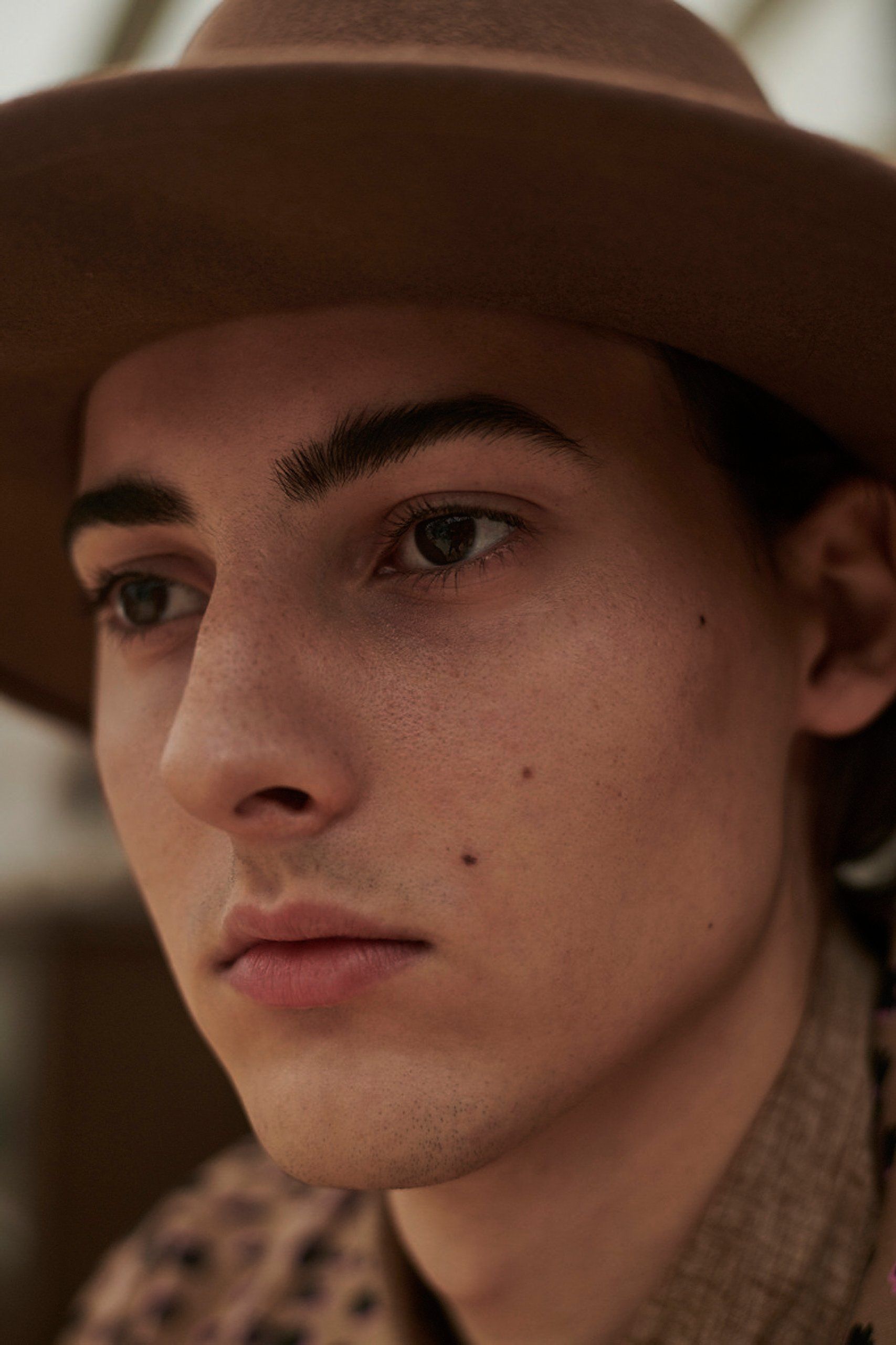 Nahaufnahme einer jungen Person mit braunem Hut und ernstem Gesichtsausdruck.