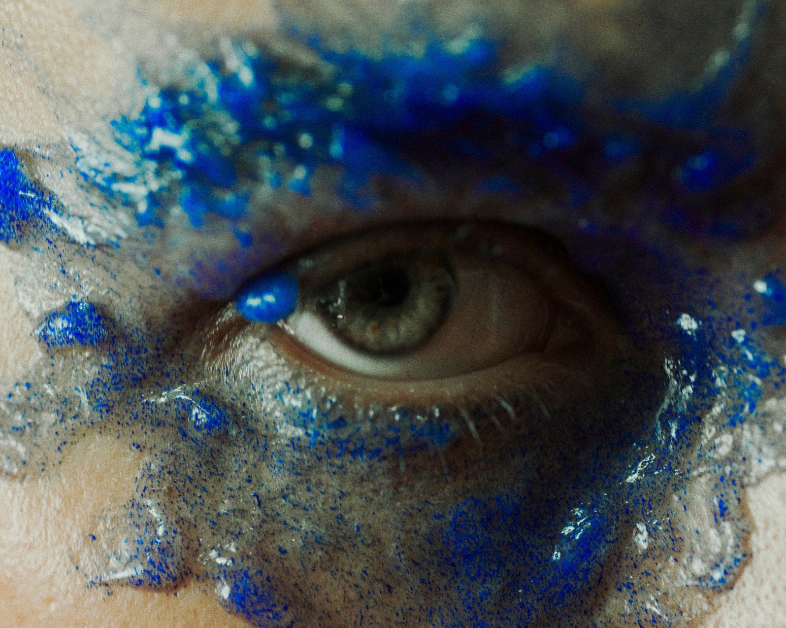 Nahaufnahme eines Auges mit blauer Farbe und Glitzer drumherum.