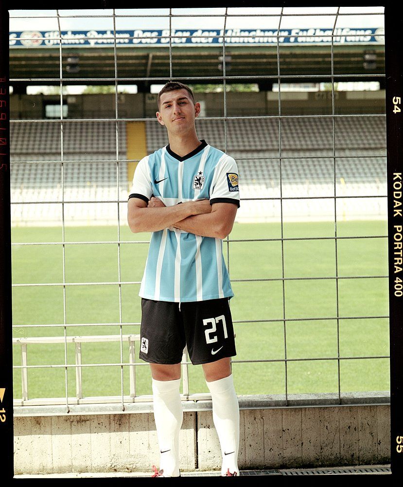 Fußballspieler in hellblauer und schwarzer Uniform, die Arme verschränkt, steht auf dem Feld im Stadion.