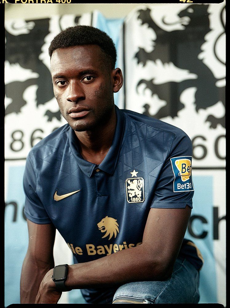 Fußballspieler im blauen Trikot, mit ernster Miene vor einem Banner lehnend.