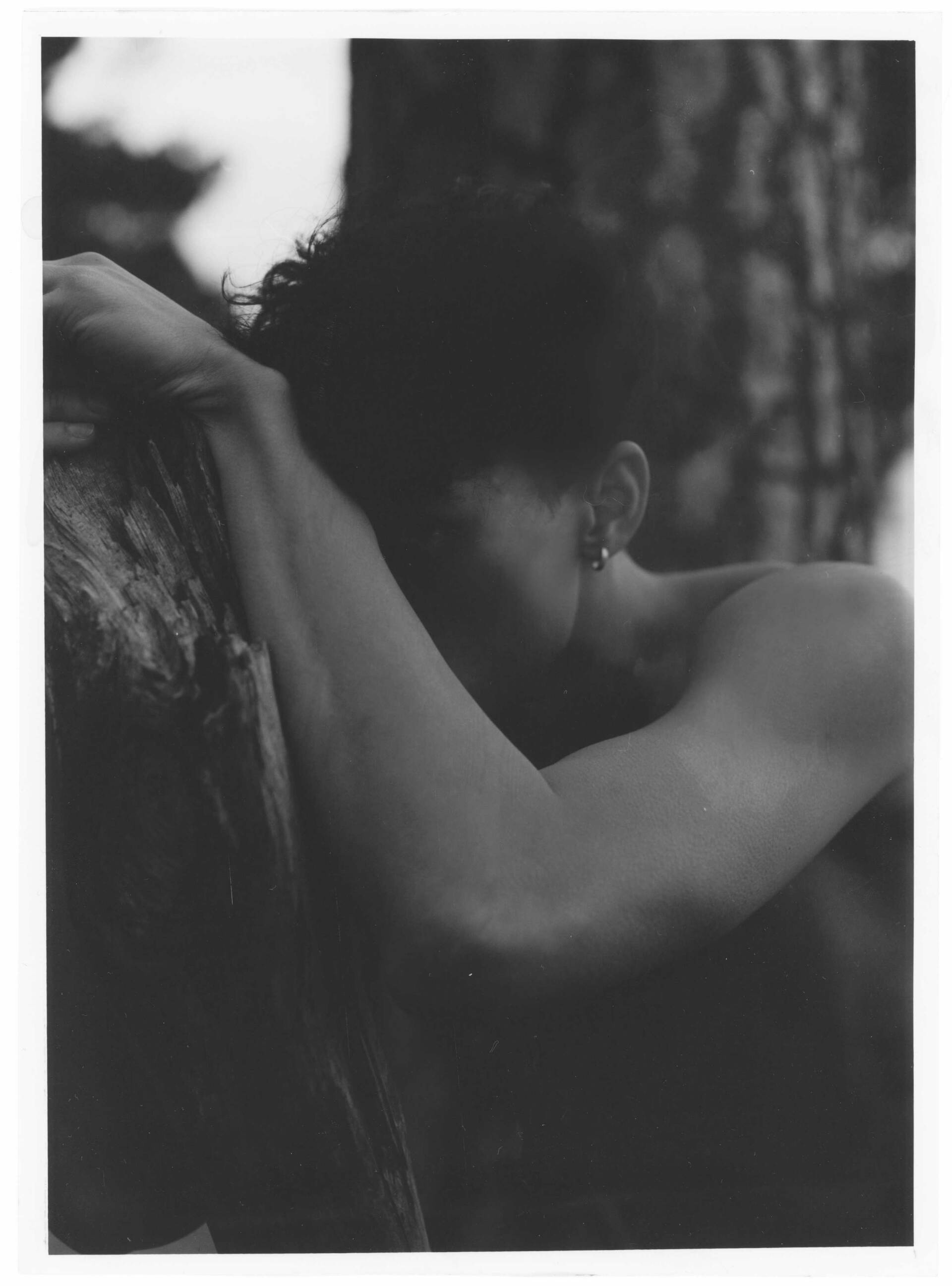 Person mit dunklem Haar lehnt an einem Baumstamm, Kopf nach unten, Arm abgestützt. Schwarz und weiß.