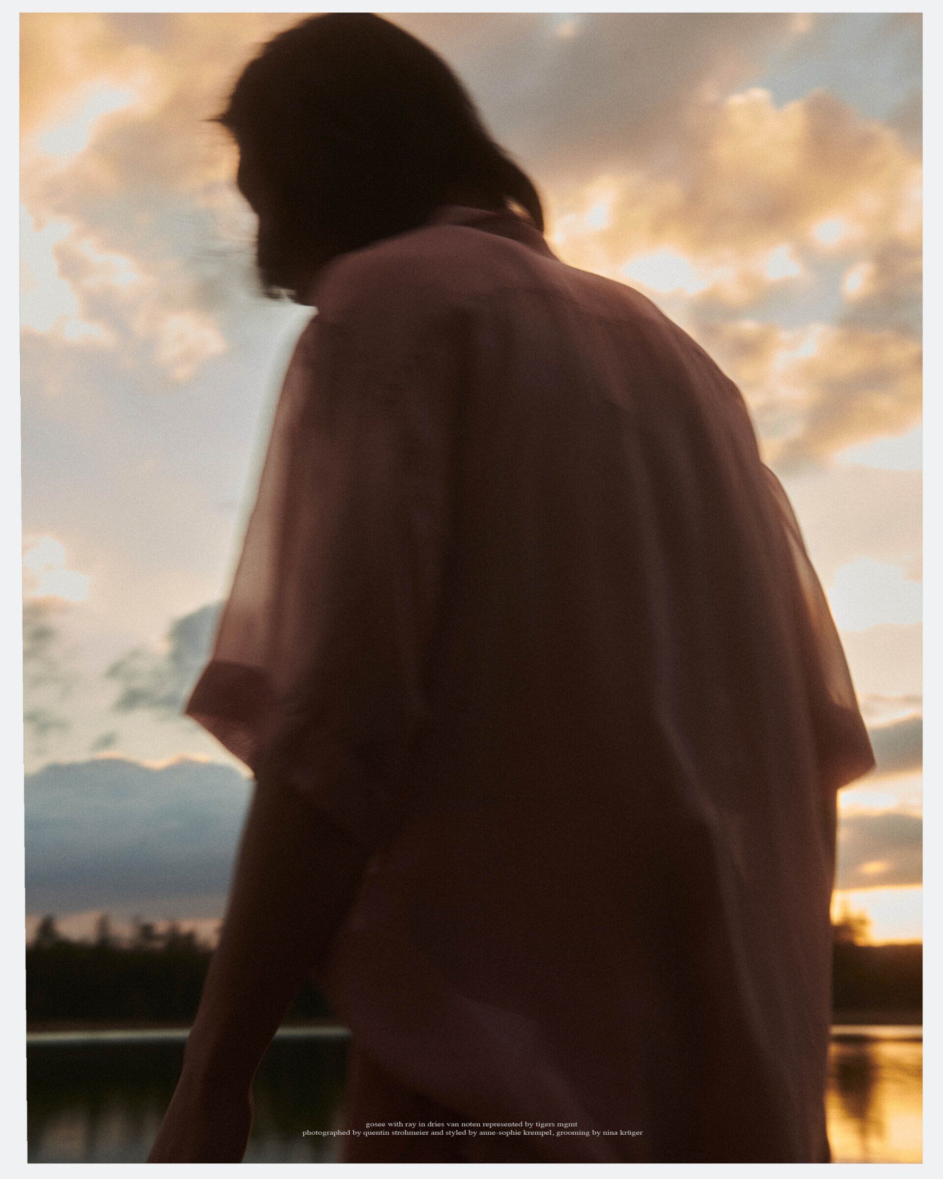 Person in einem rosa Hemd bei Sonnenuntergang mit Blick aufs Wasser. Silhouette, warme Farben.