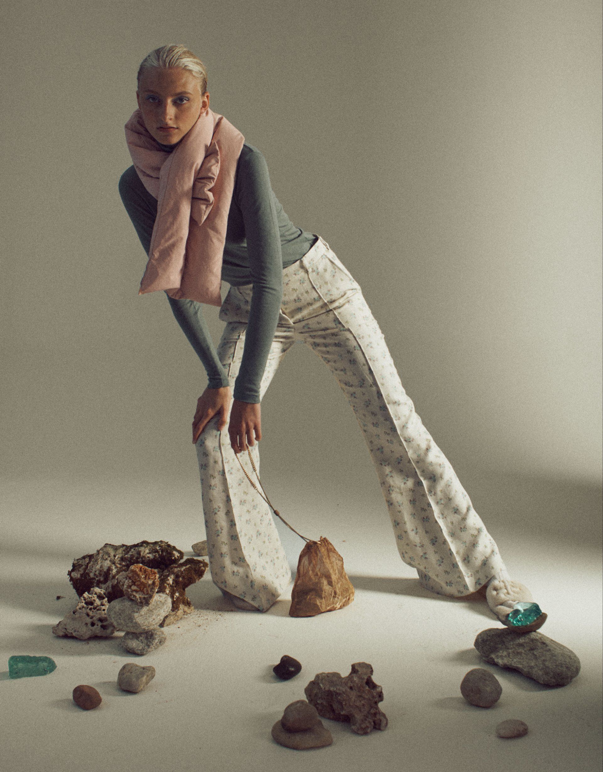 Frau in hellen Hosen und rosa Schal beugt sich über Steine auf dem Boden.