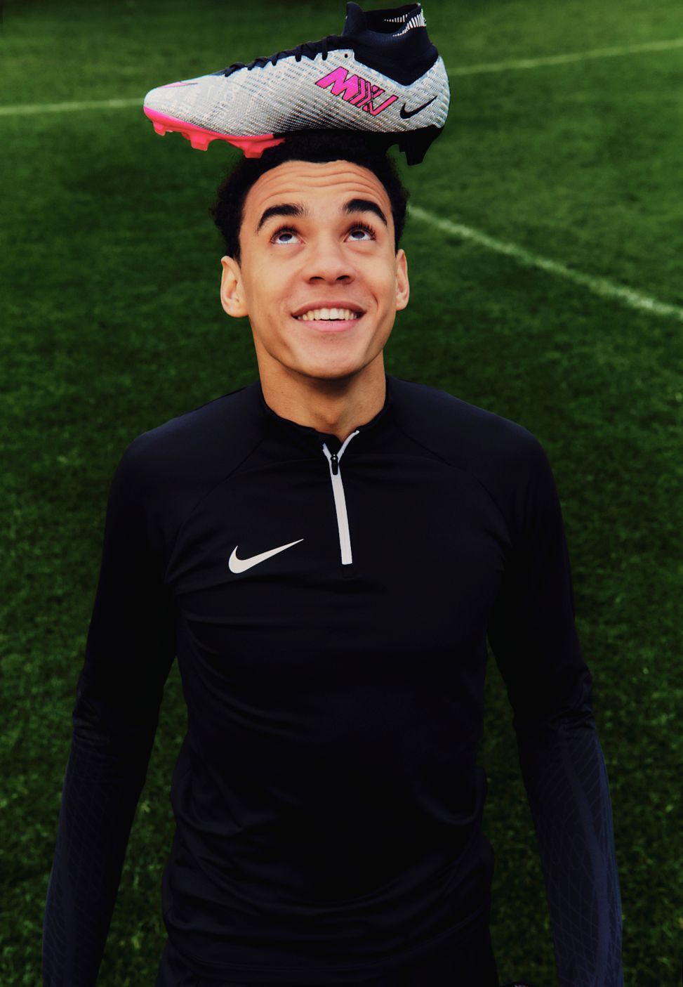 Lächelnder Mann balanciert einen Fußballschuh auf seinem Kopf auf einem grünen Feld.