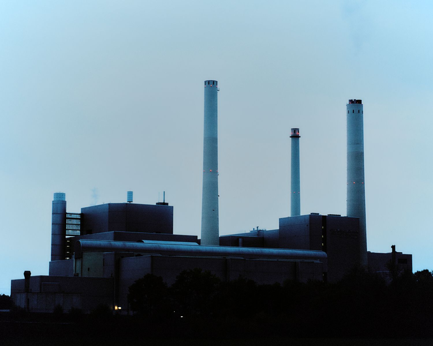 Kraftwerk in der Abenddämmerung mit hohen weißen Schornsteinen vor einem hellblauen Himmel.