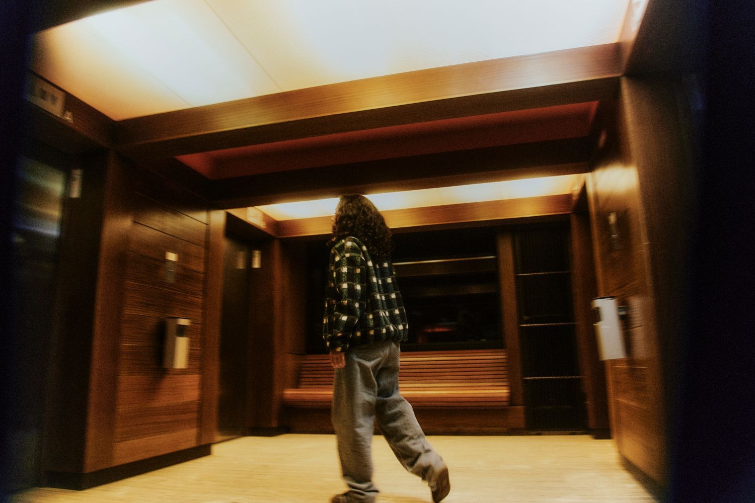 Person geht durch eine holzgetäfelte Lobby mit heller Deckenbeleuchtung.