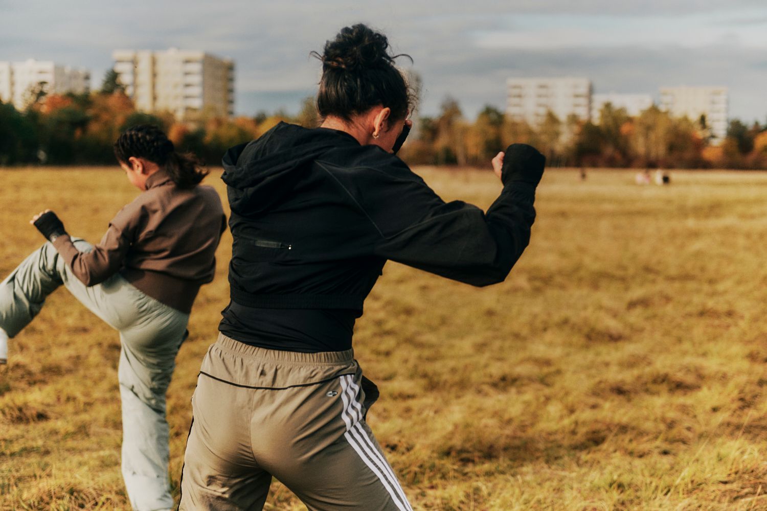 Zwei Frauen üben auf einer Wiese Kampfsport; die eine tritt, die andere schlägt.