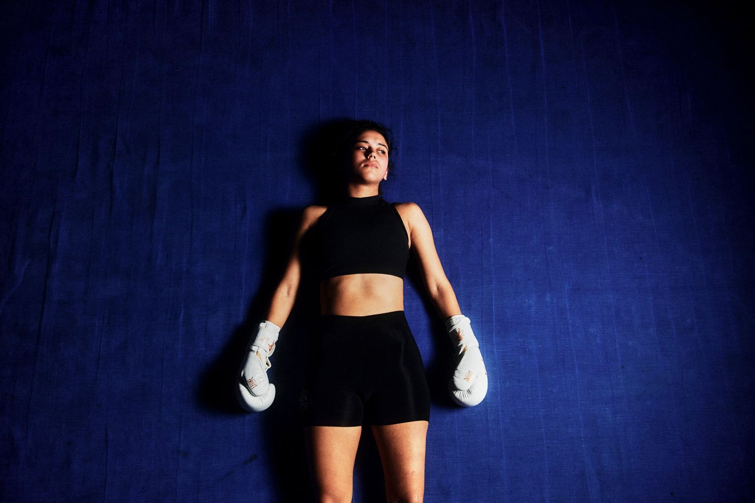 Frau in Boxausrüstung, liegt auf blauer Matte und blickt nach oben.