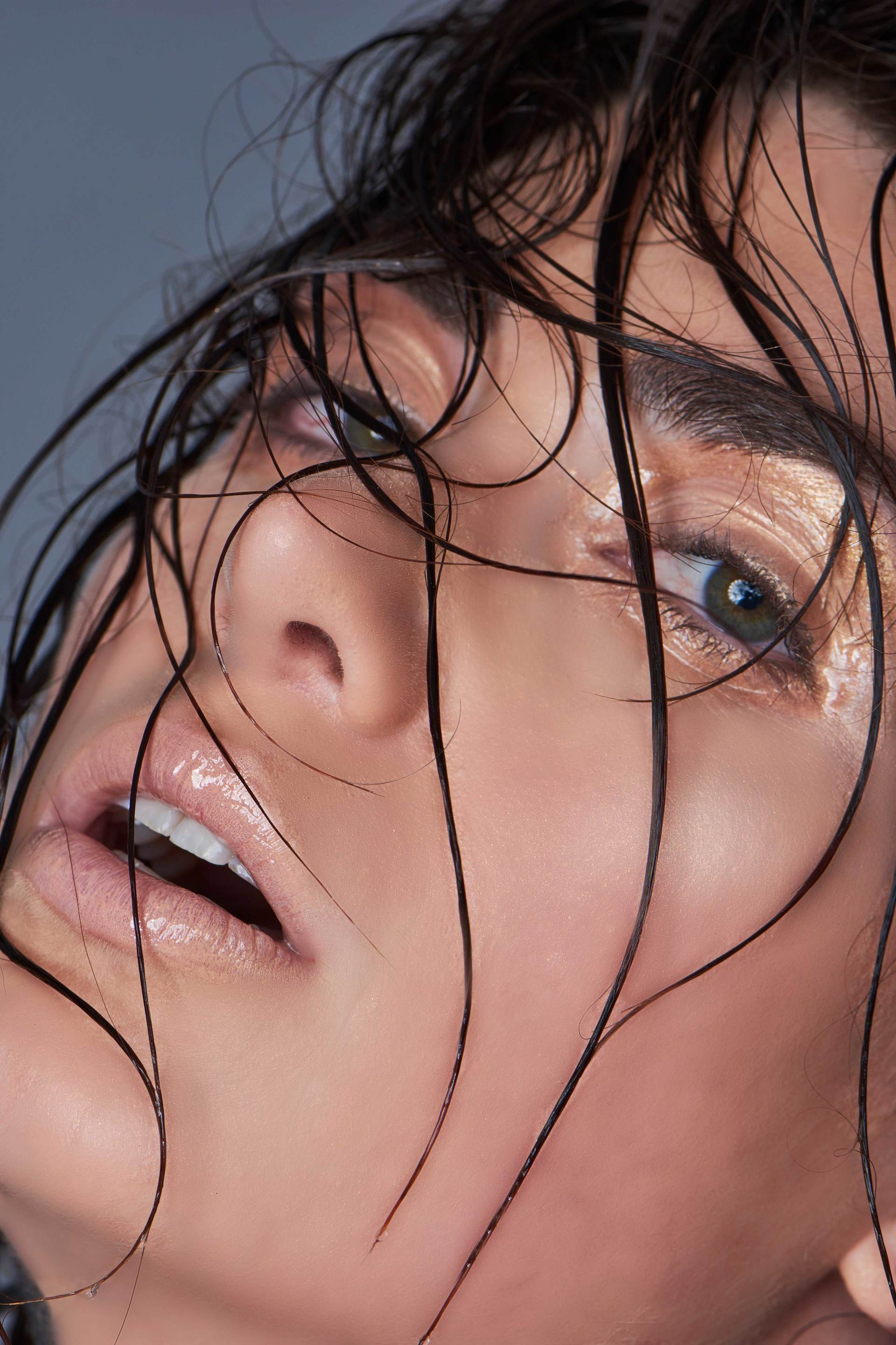 Frau mit nassem Haar, offenem Mund und goldenem Augen-Make-up, die nach oben schaut.