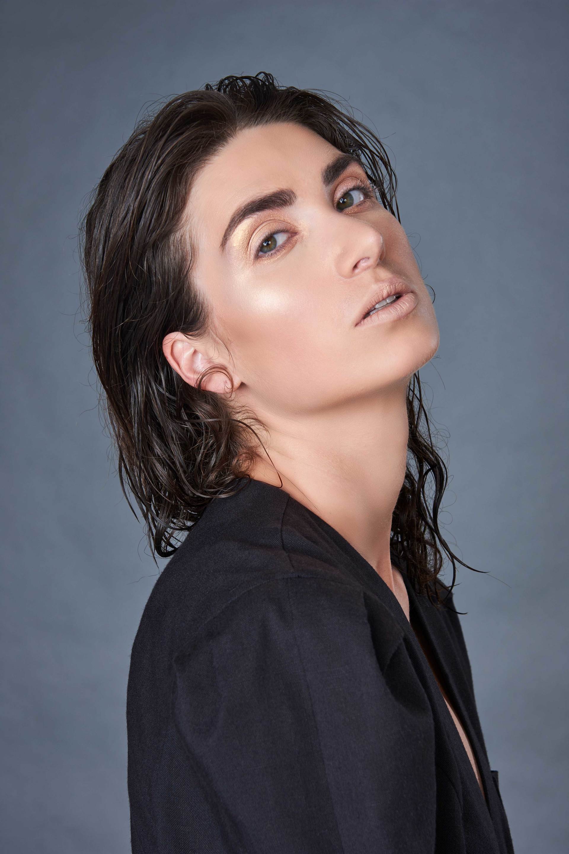 Frau mit dunklem Haar, trägt eine schwarze Jacke, blickt in die Kamera, neutraler Hintergrund.
