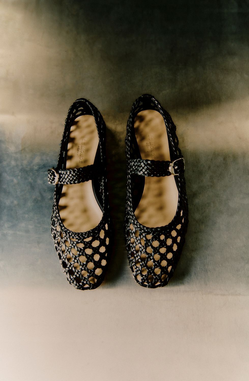 Schwarze, glitzernde Mary-Jane-Schuhe mit runden Ausschnitten vor einem Hintergrund mit Farbverlauf in Blau und Grau.