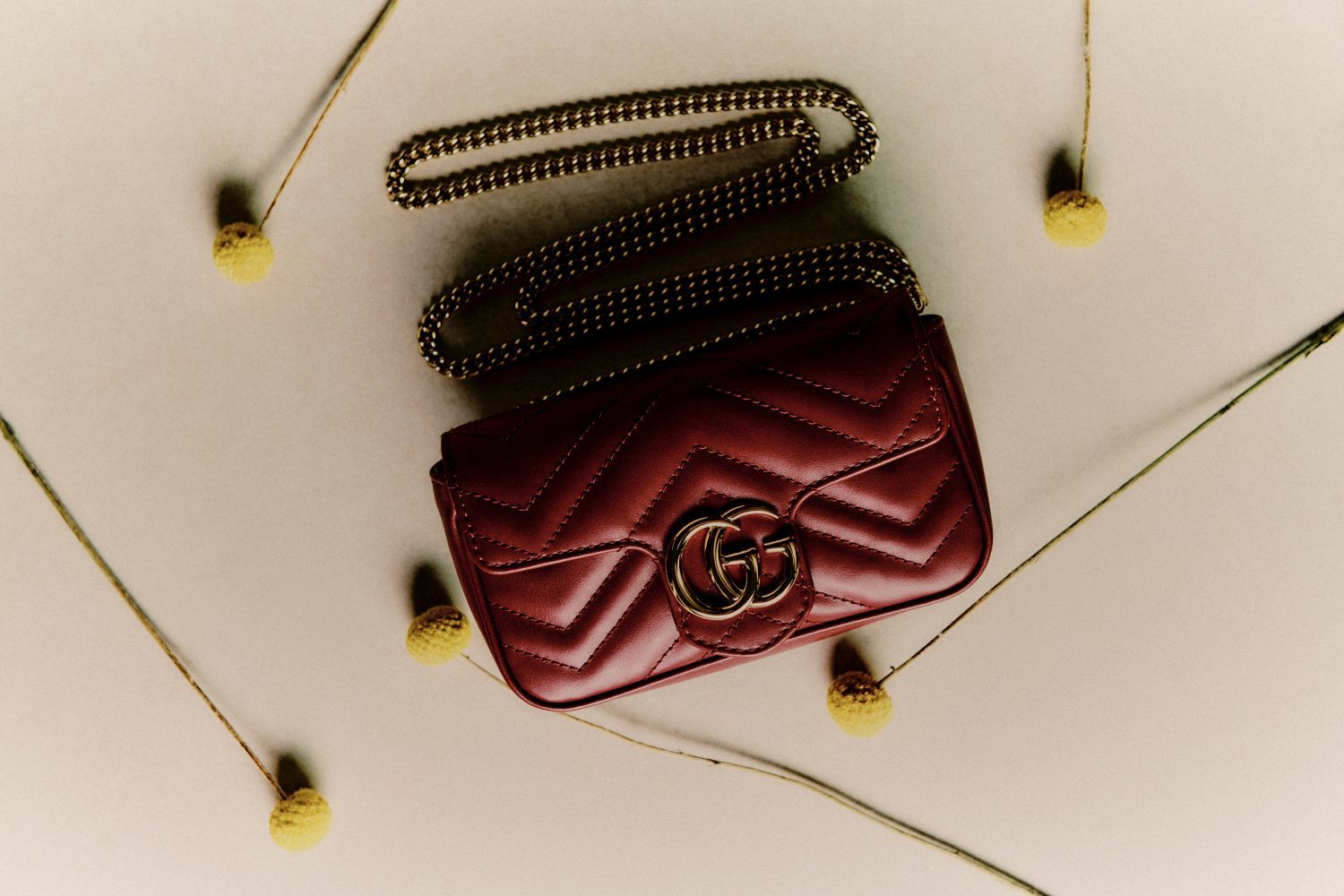 Kastanienbraune Gucci Marmont-Tasche mit Goldkette, umgeben von gelben Wildblumen.