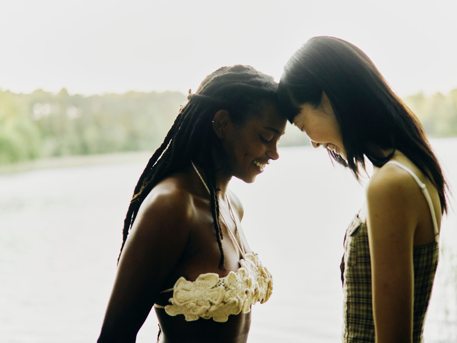 Zwei Frauen, deren Köpfe sich berühren, lächeln in der Nähe von Wasser. 
