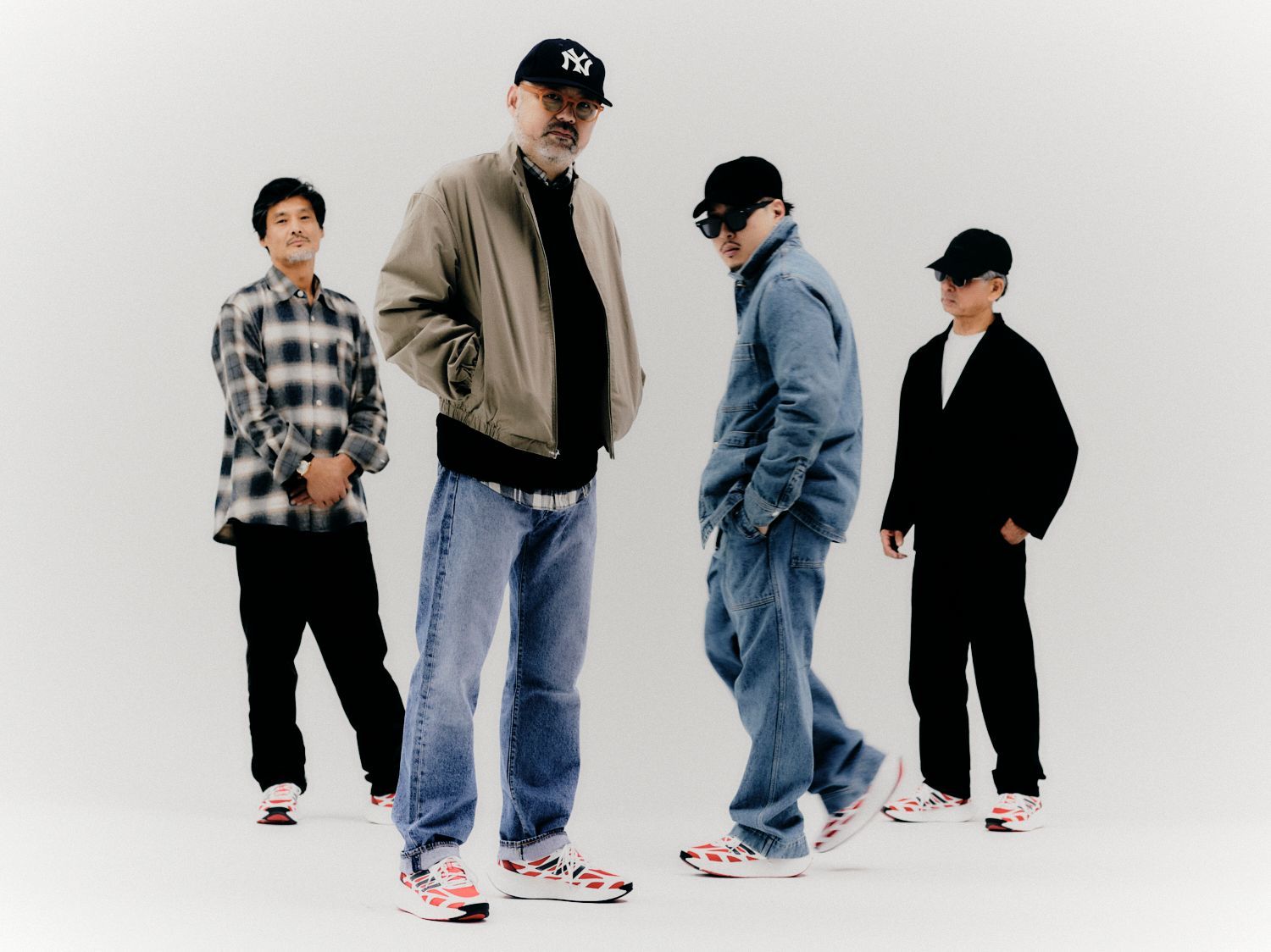 Vier Personen in Freizeitkleidung posieren; alle tragen Turnschuhe, weißer Hintergrund.