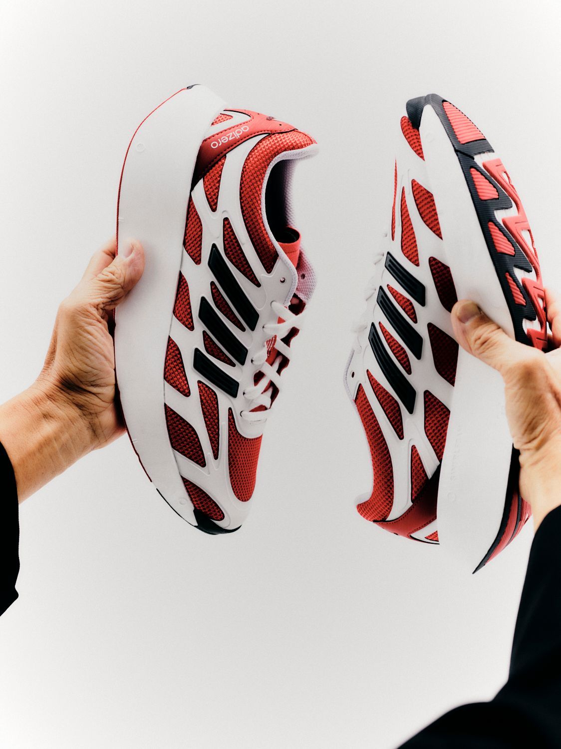 Hände halten einen aufgeschnittenen Sneaker mit rot-weißem Design vor einem weißen Hintergrund.