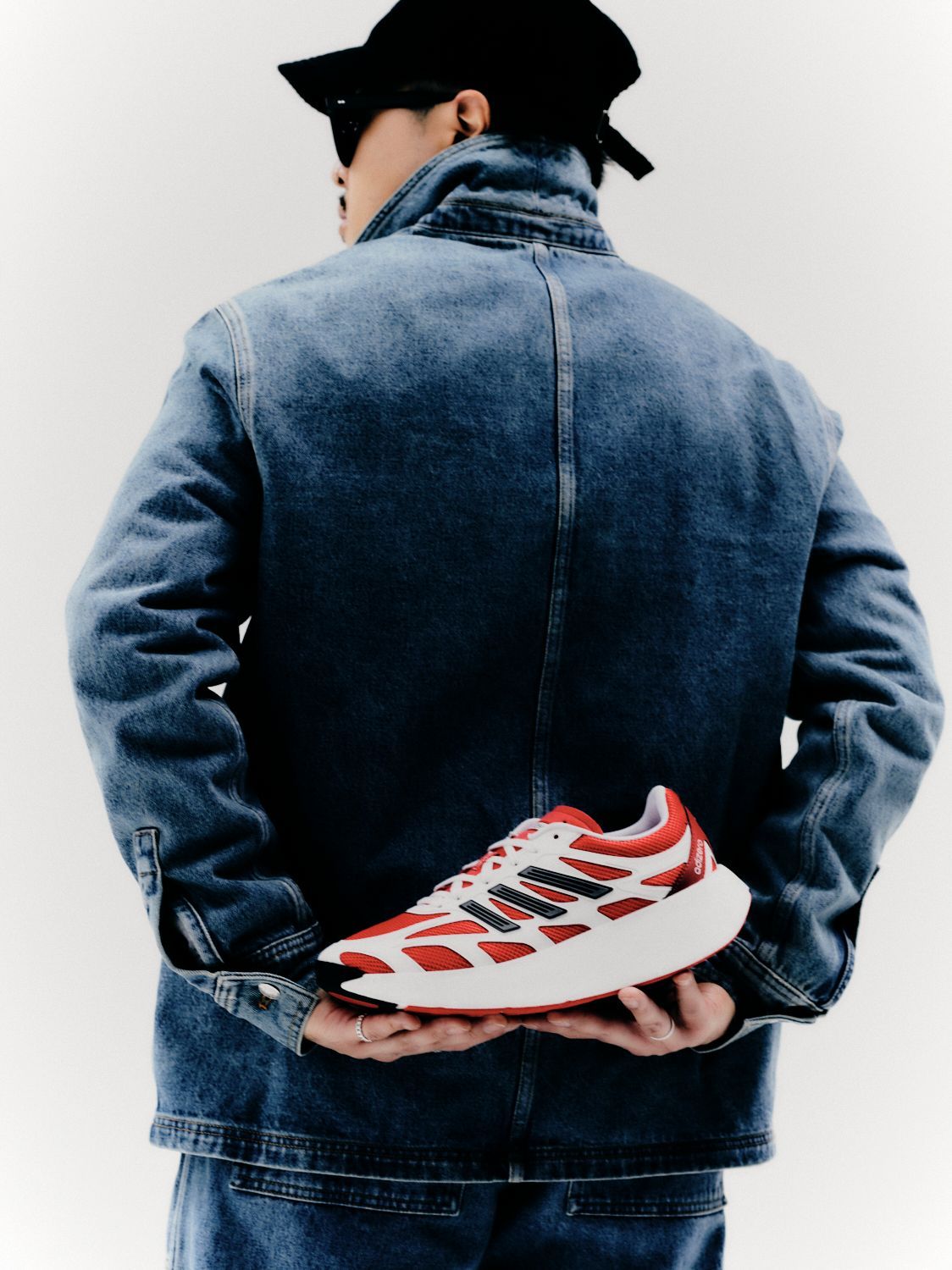 Person in Jeansjacke und Hut hält einen rot-weißen Turnschuh.