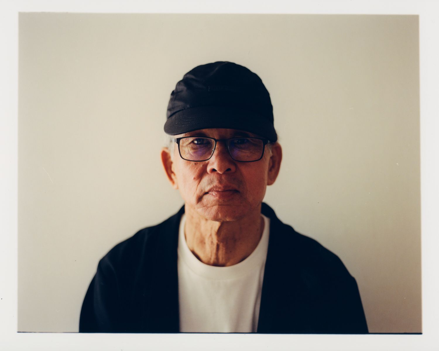 Ein älterer asiatischer Mann mit Brille und schwarzer Mütze starrt direkt in die Kamera.