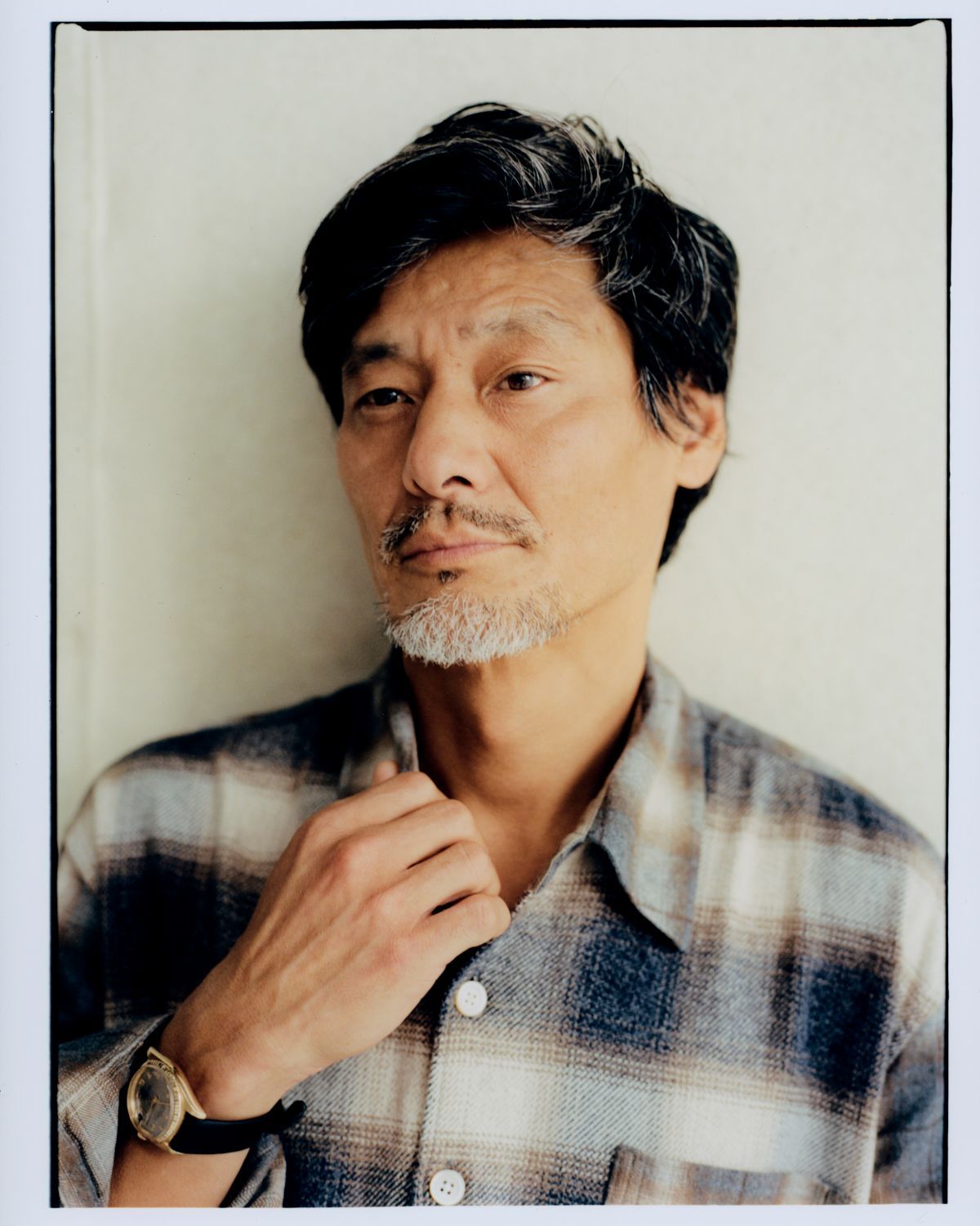 Asiatischer Mann mittleren Alters im karierten Hemd, Blick aus dem Bild, Hand am Kragen.