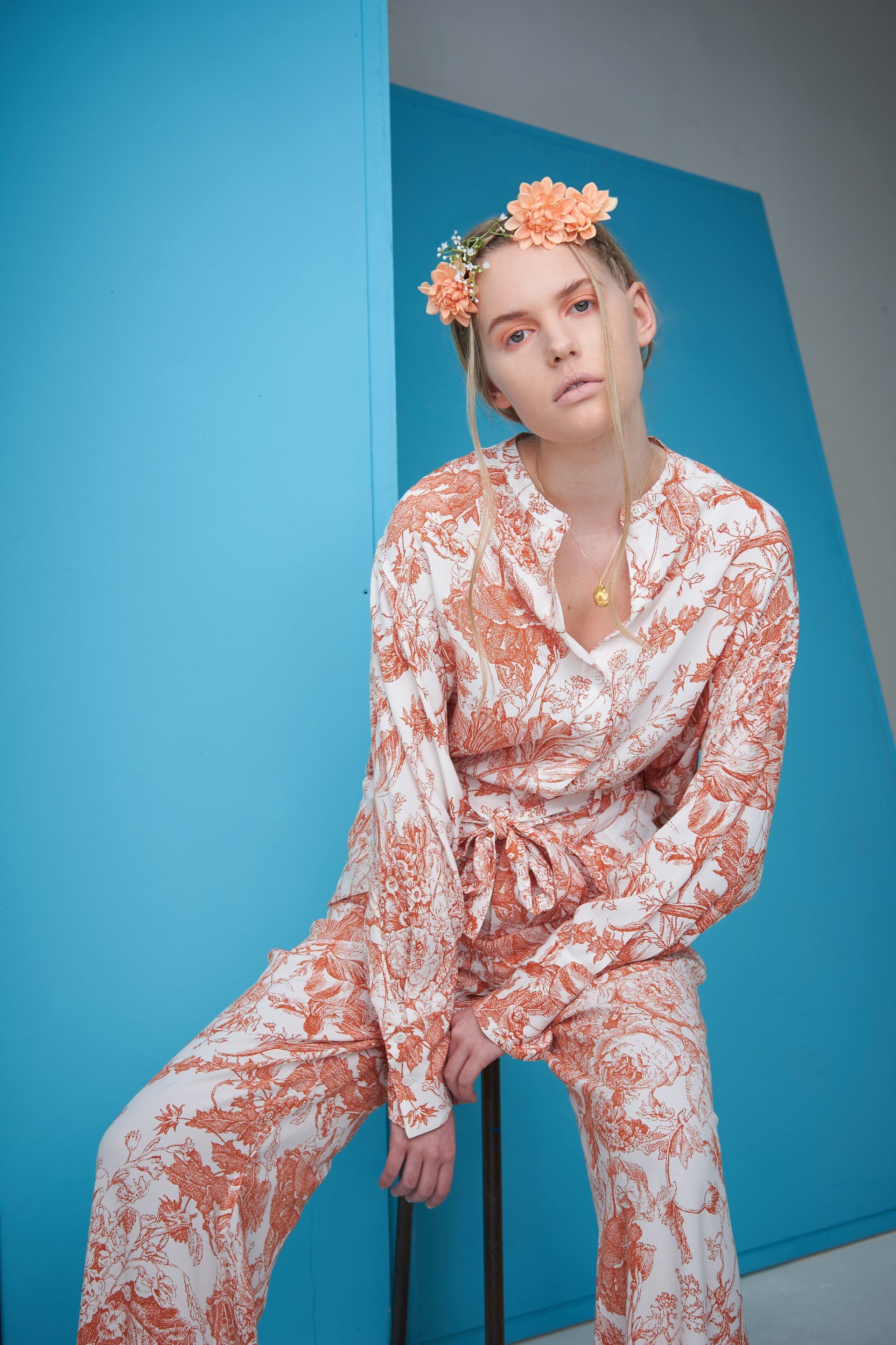 Frau in einem Outfit mit Blumenmuster und Blumenkrone posiert vor einem blauen Hintergrund.