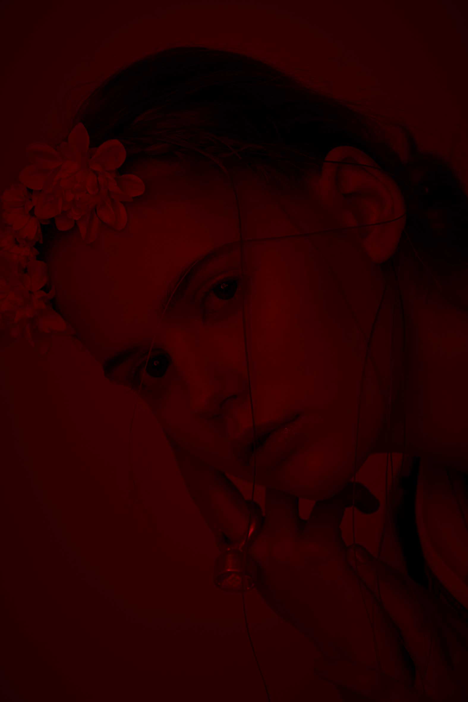 Frau mit Blumenkrone, Gesicht im Schatten, rote Beleuchtung.
