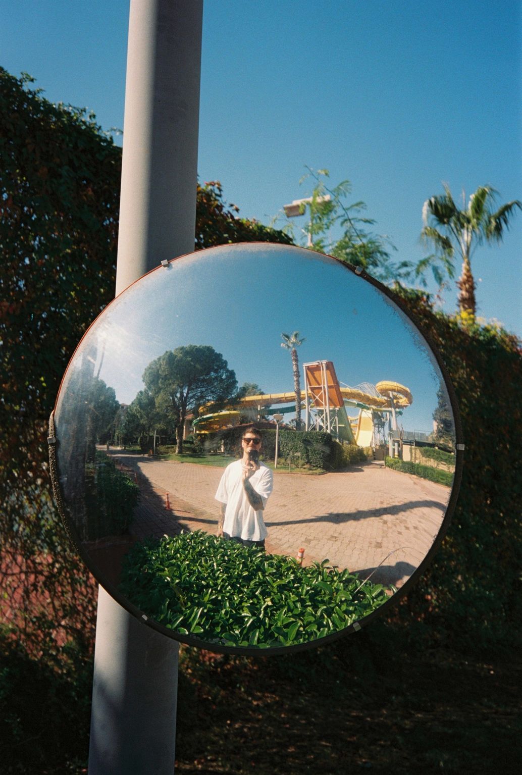 Mann mit Sonnenbrille und Tattoos hält Kamera am Strand.
