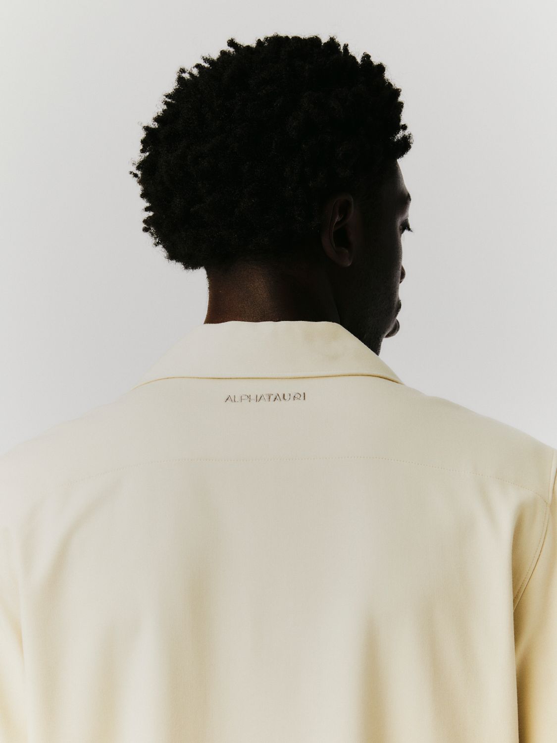 Rückansicht eines Schwarzen in einer cremefarbenen Jacke; sein Afro ist sichtbar.