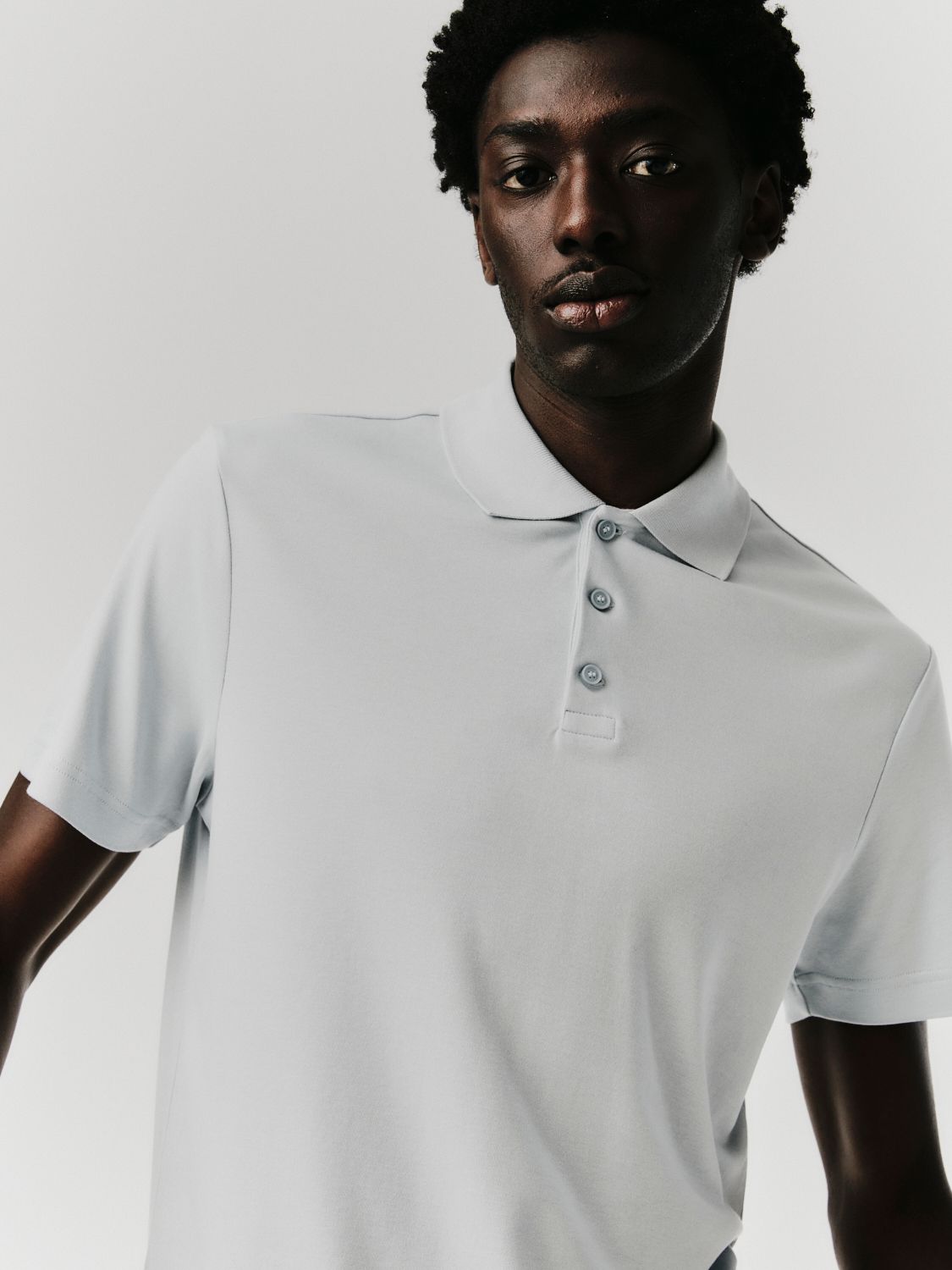 Mann in hellblauem Poloshirt, blickt zum Betrachter.