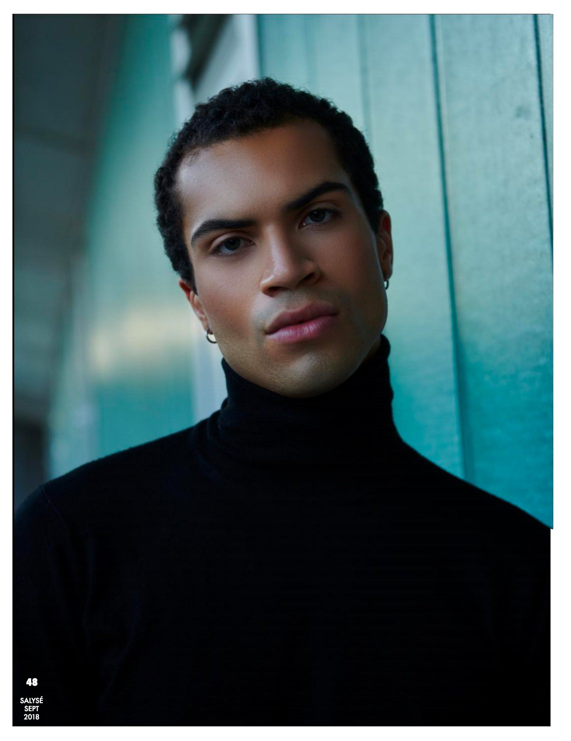 Mann im schwarzen Rollkragenpullover vor blaugrünem Hintergrund, blickt in die Kamera.