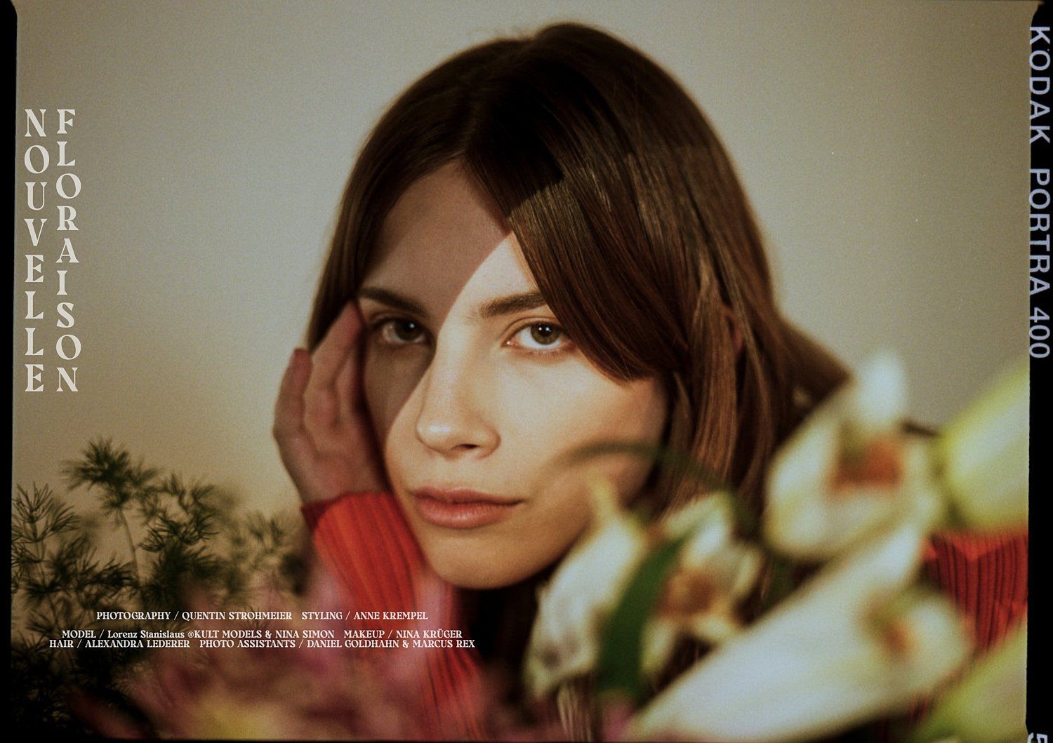 Frau mit dunklem Haar und rotem Pullover hält ihr Gesicht, umgeben von Blumen, warme Töne.