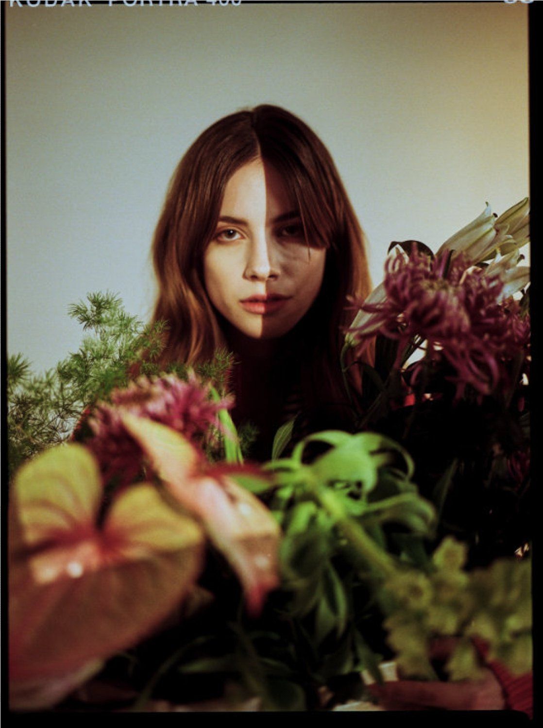 Frau, deren Gesicht zur Hälfte im Schatten liegt, umgeben von Blumen und Grün.