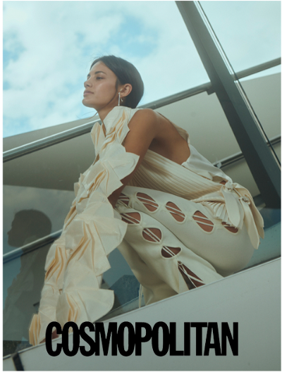 Frau in weißem, ausgeschnittenem Outfit posiert auf einer modernen Treppe. Heller Hintergrund, Blick nach oben. 